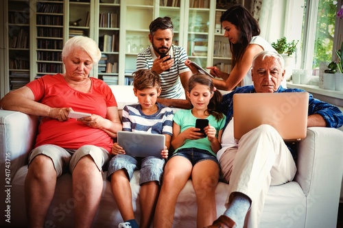Multi-generation family sitting on sofa and using various