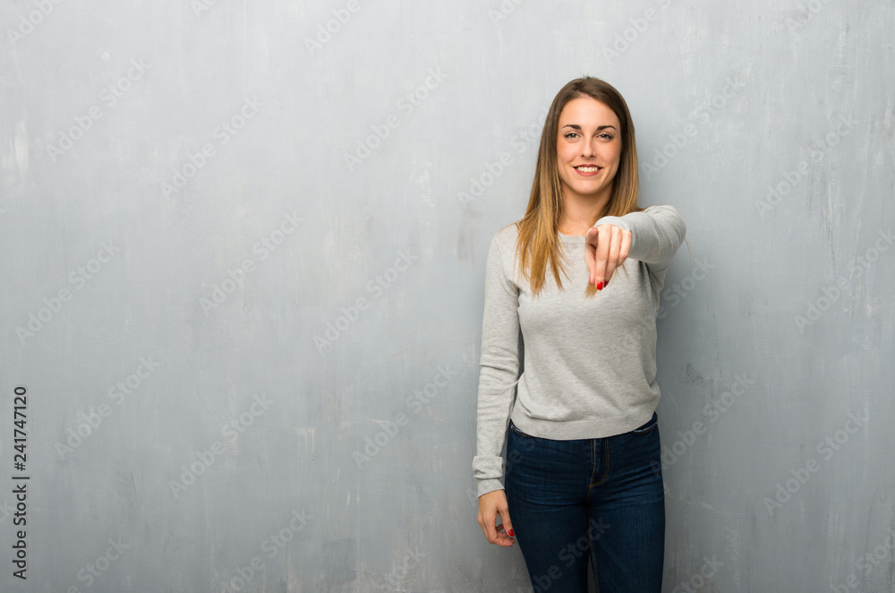 Young woman on textured wall points finger at you with a confident expression Young woman on textured wall points finger at you with a confident expression