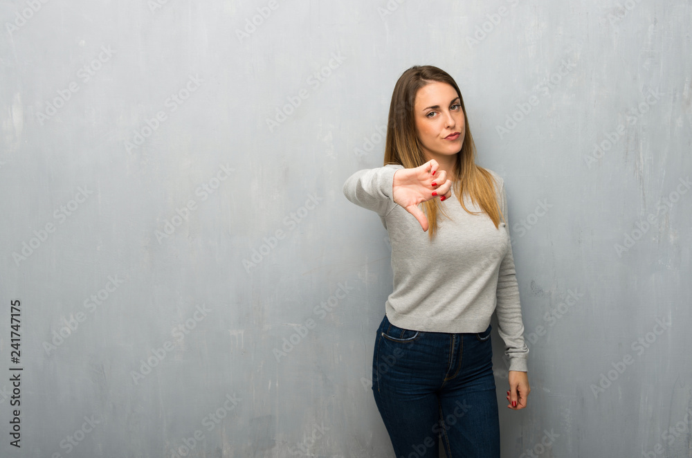 Young woman on textured wall showing thumb down sign with negative expression Young woman on textured wall showing thumb down sign with negative expression