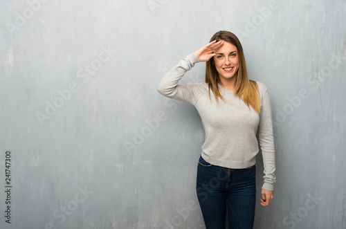 Young woman on textured wall saluting with hand