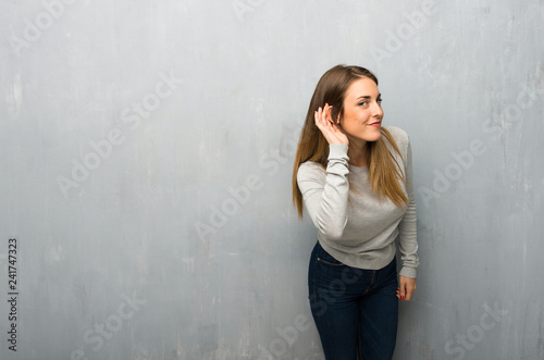 Young woman on textured wall listening to something by putting hand on the ear