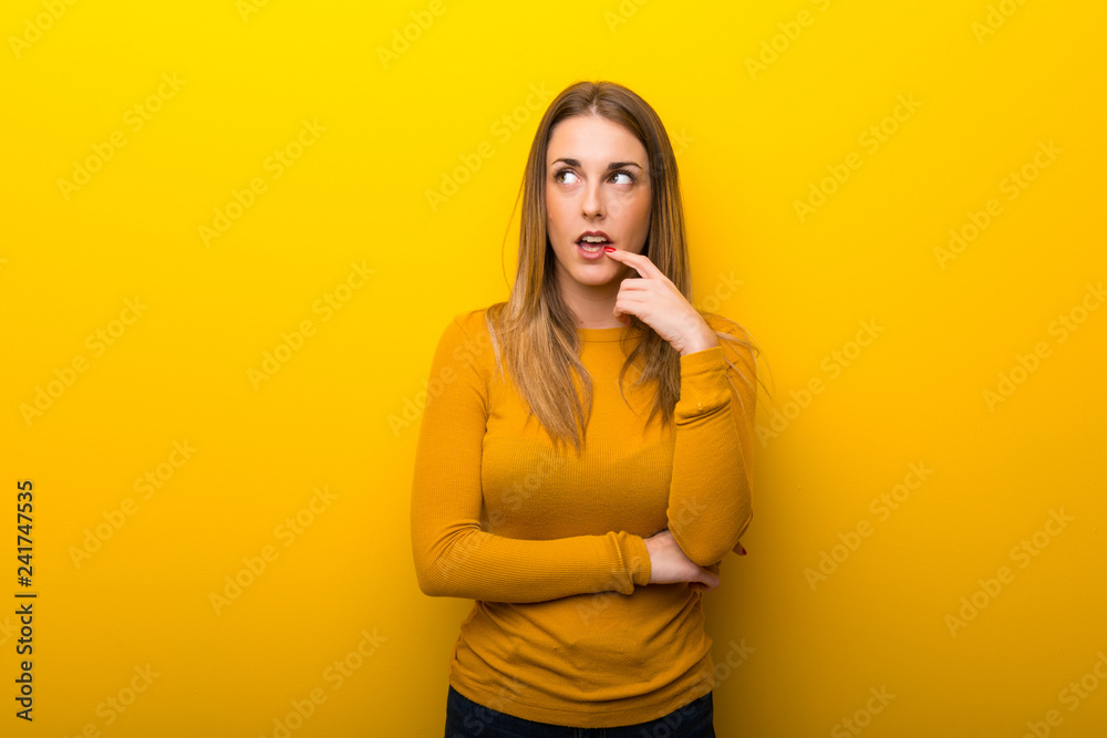 Young woman on yellow background having doubts while looking up Young woman on yellow background having doubts while looking up