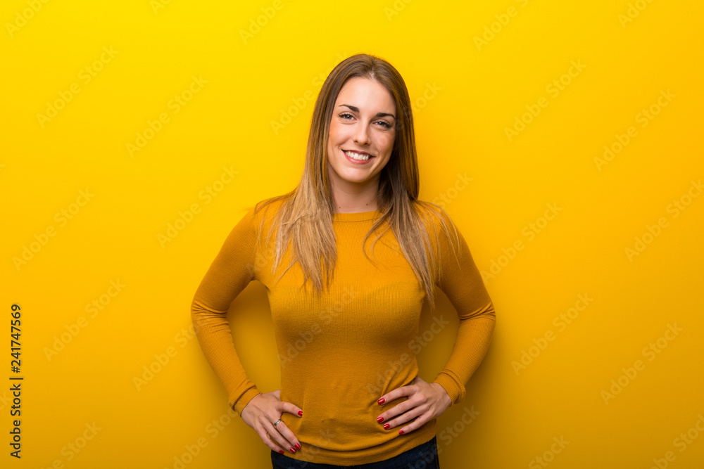 Obraz premium Young woman on yellow background posing with arms at hip and laughing looking to the front