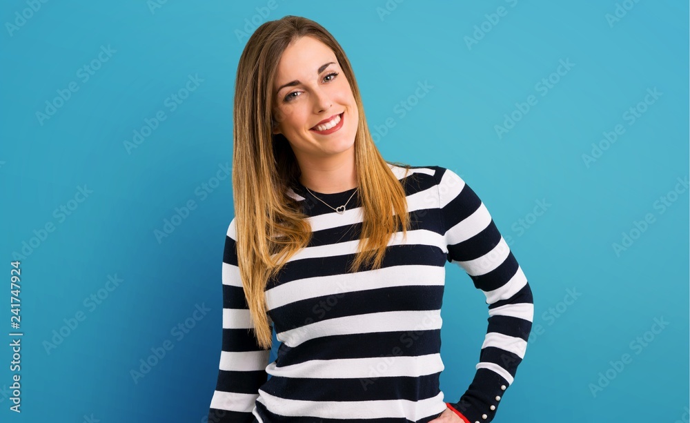 Blonde youn girl posing with arms at hip on blue background Blonde youn girl posing with arms at hip on blue background