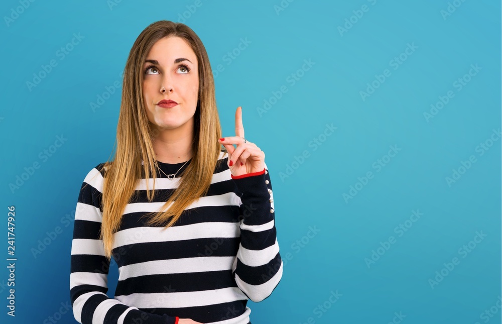 Blonde youn girl standing and thinking an idea on blue background Blonde youn girl standing and thinking an idea on blue background