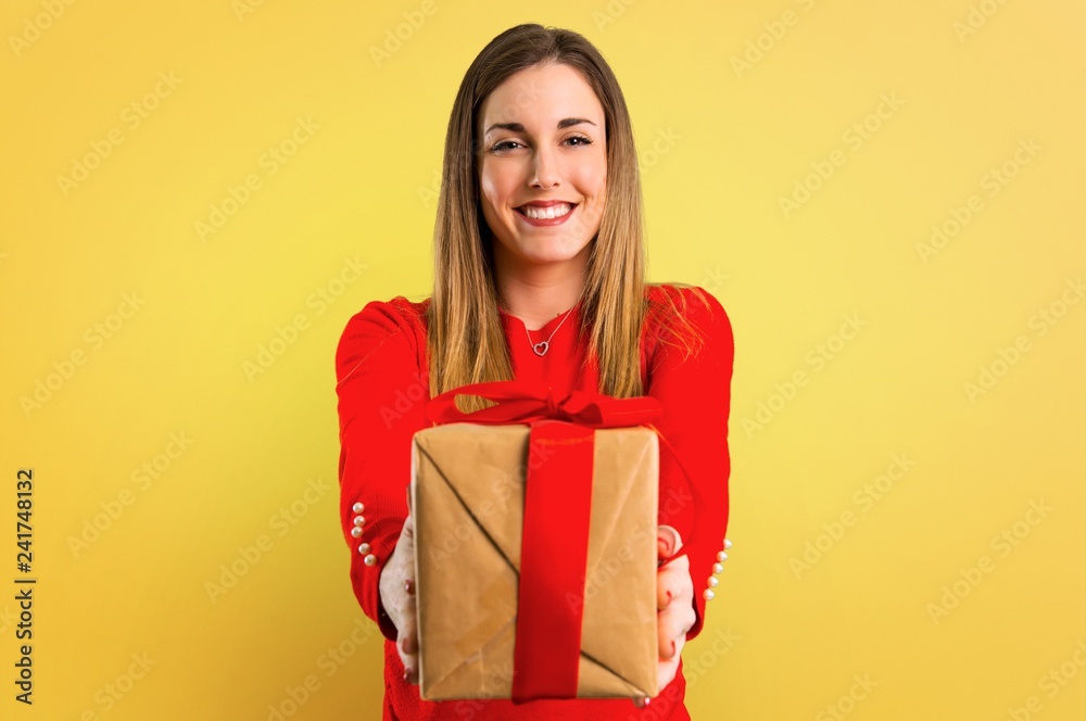 Happy Young blonde woman holding a gift on yellow background Happy Young blonde woman holding a gift on yellow background
