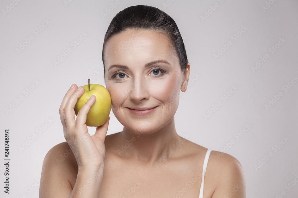 Portrait of charming beautiful healthy caucasian middle aged woman holding green apple, she love to eat fruit, make her get good health, nice skin, lose weight and weight control. Copy space, indoor Portrait of charming beautiful healthy caucasian middle aged woman holding green apple, she love to eat fruit, make her get good health, nice skin, lose weight and weight control. Copy space, indoor