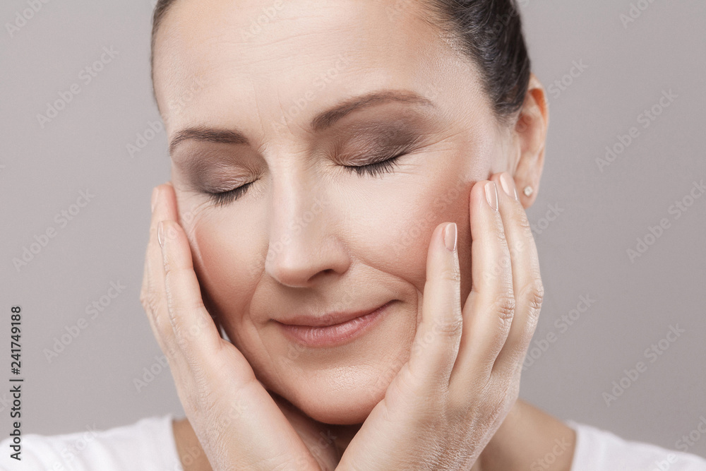 Portrait of satisfied middle aged woman with perfect face skin relaxation after spa procedure with closed eyes isolated on grey background. Beauty and skin care concept,copy space, studio shot, indoor Portrait of satisfied middle aged woman with perfect face skin relaxation after spa procedure with closed eyes isolated on grey background. Beauty and skin care concept,copy space, studio shot, indoor