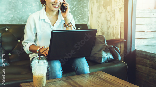 Asian woman sitting relax on the sofa Is talking on a mobile phone and is working with a notebook. at a coffee shop.