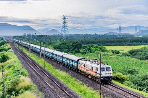 awesome close front engine view of indian railway running on track goes to horizon in green landscape under blue sky with clouds.