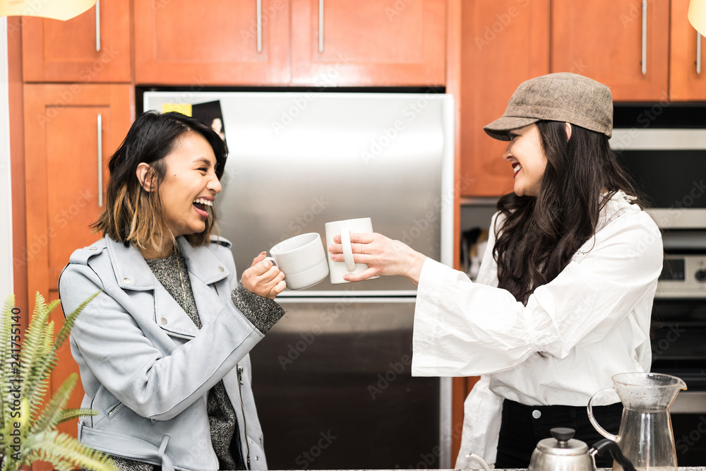 Smiling women toasting coffee cups while standing in kitchen Smiling women toasting coffee cups while standing in kitchen