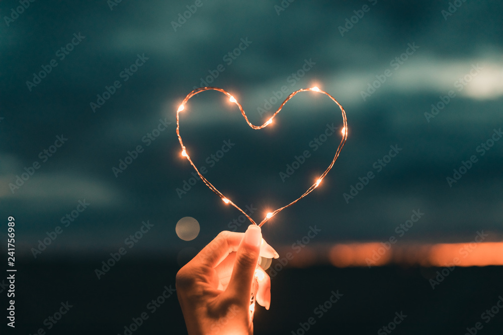 Foto Stock Simbolo del cuore fatto da una striscia di luci led tenuto da  una mano di una ragazza di fronte al cielo sfuocato. San Valentino  concetto. | Adobe Stock