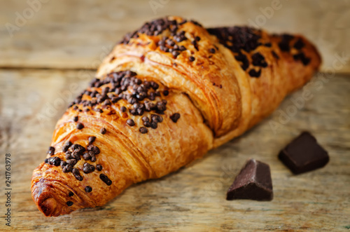 Fresh chocolate croissant with chocolate sprinkles on a wood background