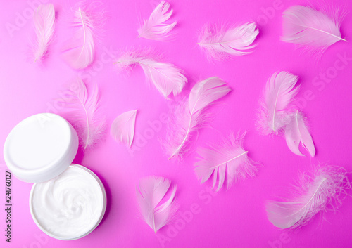 White jar cream and feather tenderness beauty on a pink background, top view