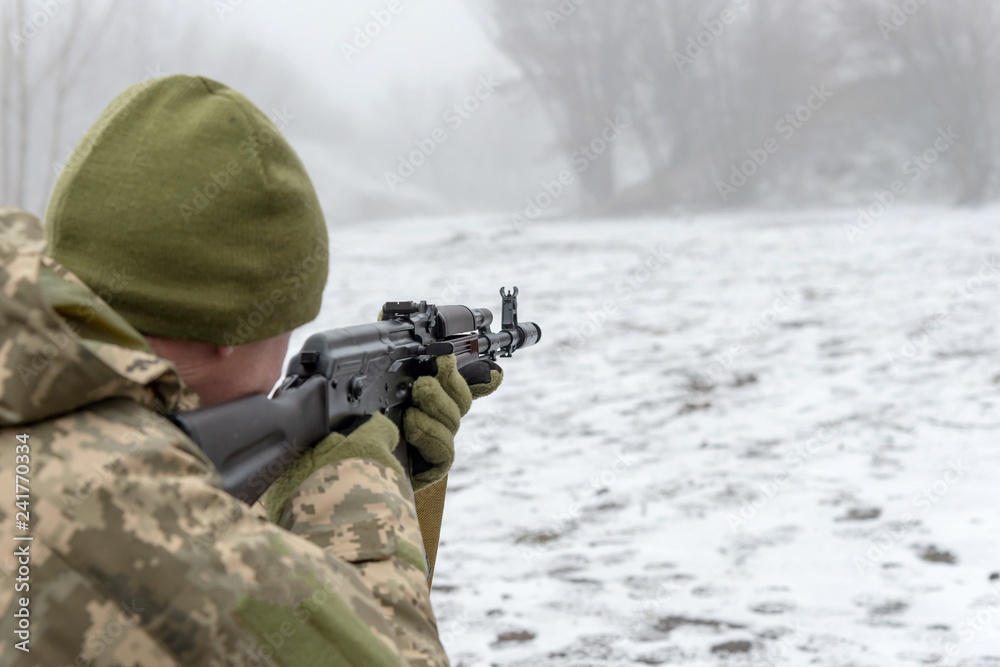 A military soldier takes aim with an automatic rifle and holds it in his mittens in winter. A military soldier takes aim with an automatic rifle and holds it in his mittens in winter.