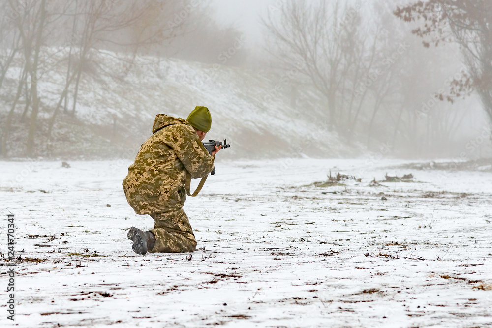 Naklejka premium A military soldier in camouflage with a weapon goes on the offensive in winter.