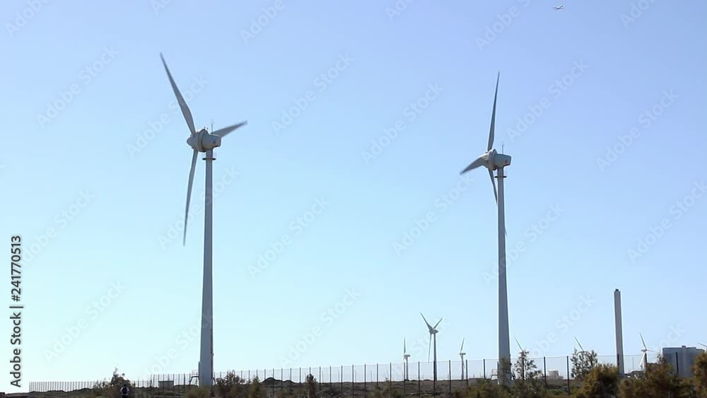 Wind turbines spinning with airplane over blue sky in Pozo Izquierdo, Gran Canaria island. Renewable energy, sustainable environment concepts in Canary Islands, Spain
