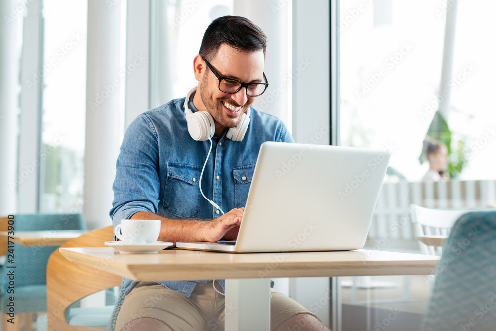 Happy man drinking coffee and looking at his laptop. - Image