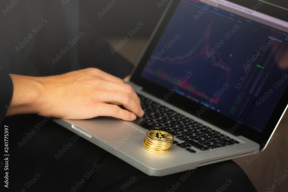 Businessman working on laptop with a golden bitcoin coins stack on it. Exchange chart on screen. Businessman working on laptop with a golden bitcoin coins stack on it. Exchange chart on screen.