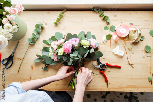 Close-up of hand Professional florist making a bouquet of pink Ranunculus and peonies in a flower shop. Arrangement and packaging of the bouquet. The concept of flower delivery and online store photo