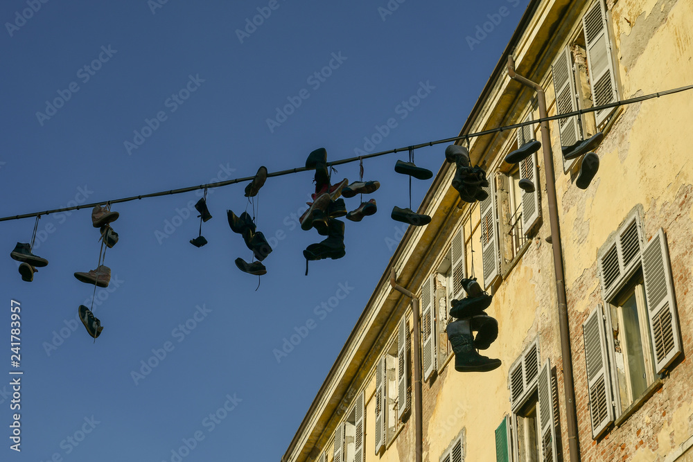 Old shoes hanging on electrical wire between ancient buildings with clear sky background, Turin, Piedmont, Italy