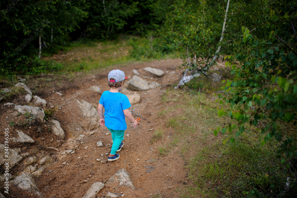 The back of a 6-years blond boy running on the top of a rocky the mountain The back of a 6-years blond boy running on the top of a rocky the mountain