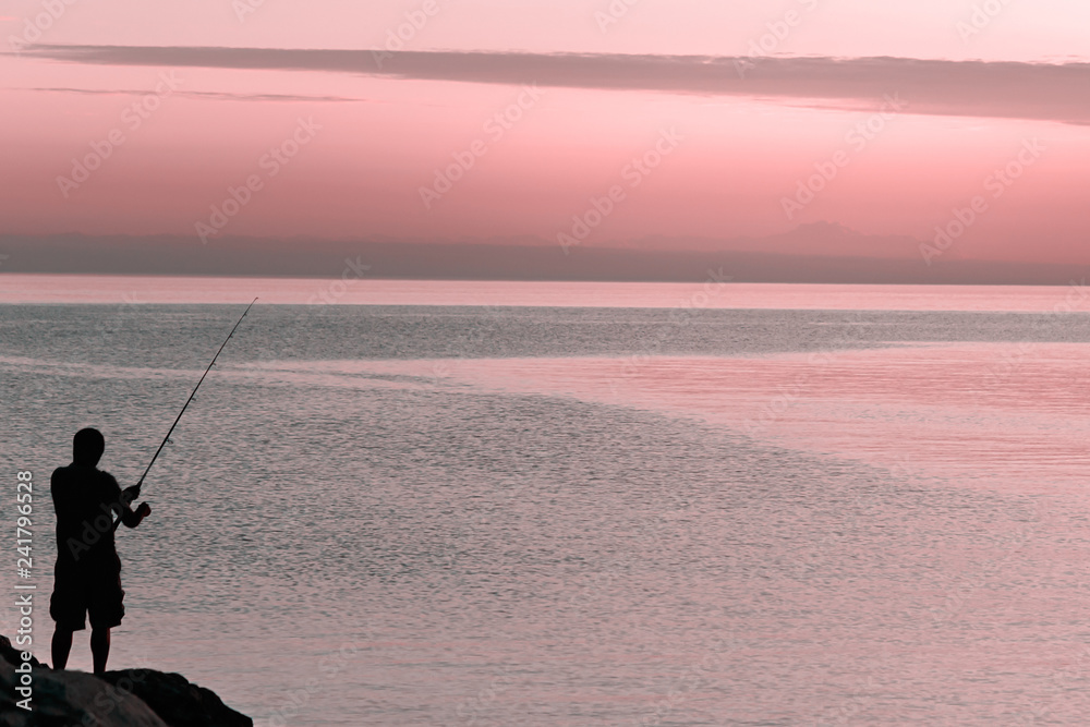 Silhouette of man with fishing spinning. Fishing on the lake at sunset Silhouette of man with fishing spinning. Fishing on the lake at sunset
