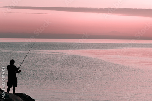 Silhouette of man with fishing spinning. Fishing on the lake at sunset