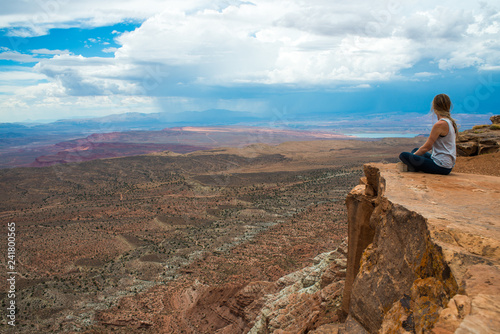 Girl sitting near the edge of a high cliff, looking outward. Southern Utah