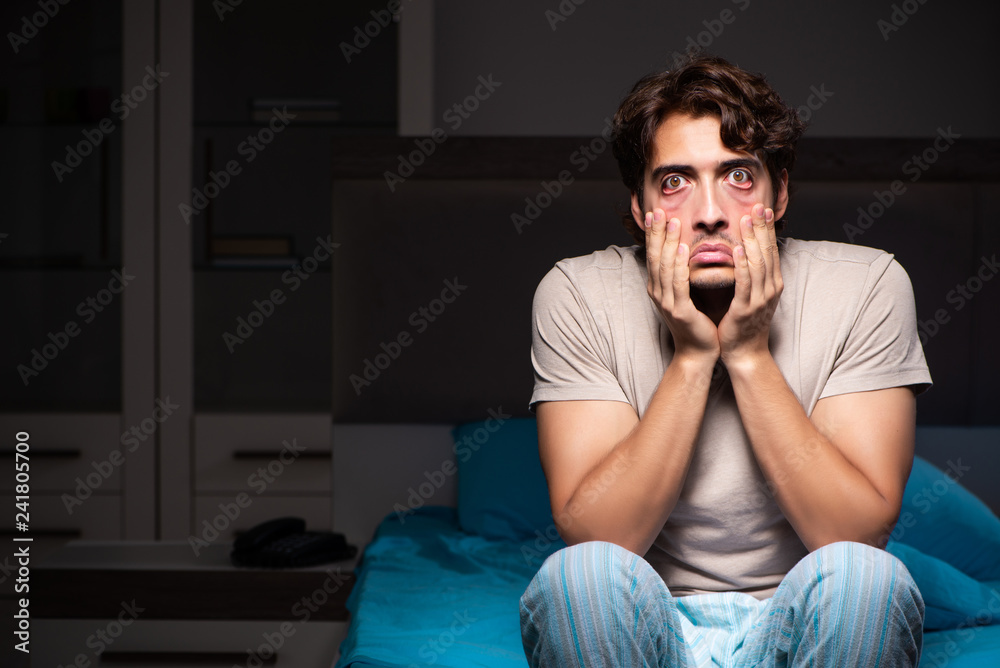 Young handsome man suffering from insomnia in bed