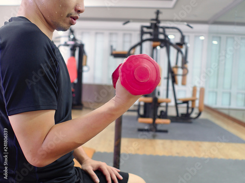 Fit young Asian man lifting dumbbell at sport gym. Fitness and workout concept