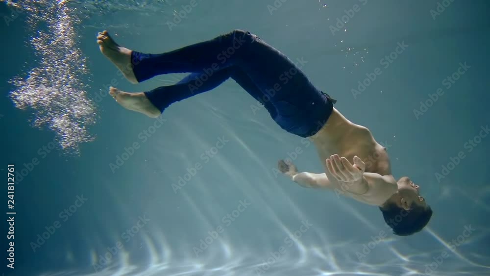 sinking man is falling to bottom of swimming pool, he is lowering to floor, moving hands and legs