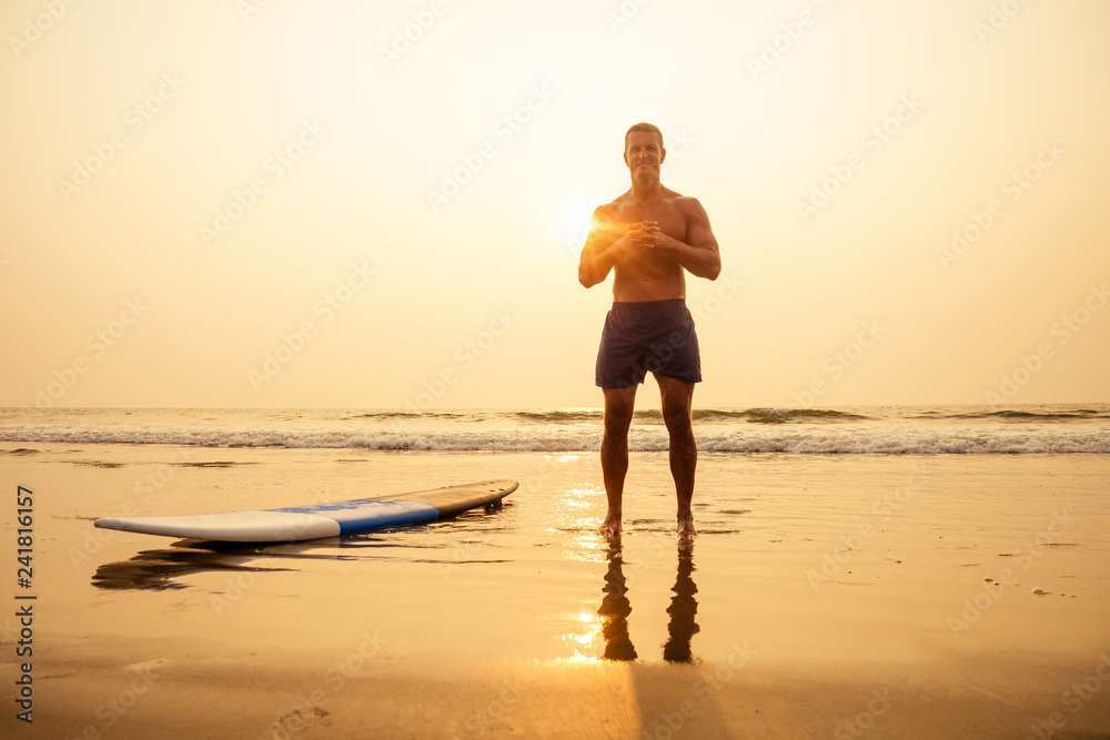 Surfer fitness male with a muscular body with his surfboard at the beach warm up.