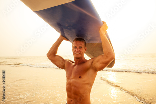 Photography Handsome active sporty man carrying his surfboard on the head