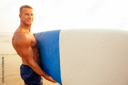 surfing freelancing man muscle and press sport training on the beach at sunset.male fitness model surfer with a big surf board near the indian ocean goa Ashwem Arambol beach photo