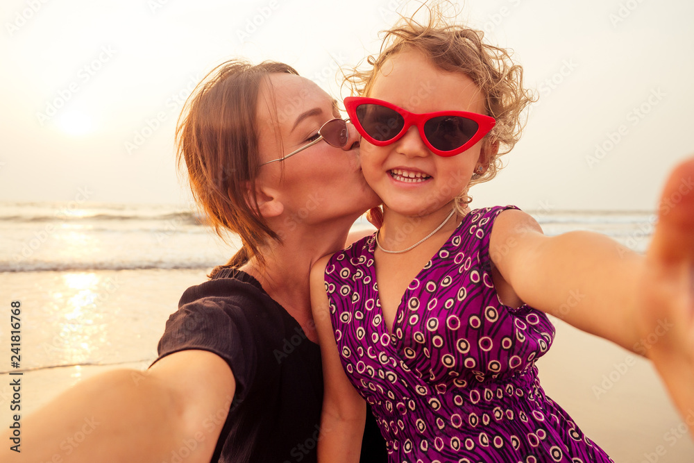 Happy stylishly mother and daughter taking selfie at sandy beach on a sunset.mothers Day.little girl blonde and beautiful woman taking pictures on the phone tourism abroad online video calling Happy stylishly mother and daughter taking selfie at sandy beach on a sunset.mothers Day.little girl blonde and beautiful woman taking pictures on the phone tourism abroad online video calling