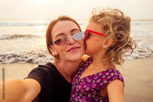 Happy stylishly mother and daughter taking selfie at sandy beach on a sunset.mothers Day.little girl blonde and beautiful woman taking pictures on the phone tourism abroad online video calling