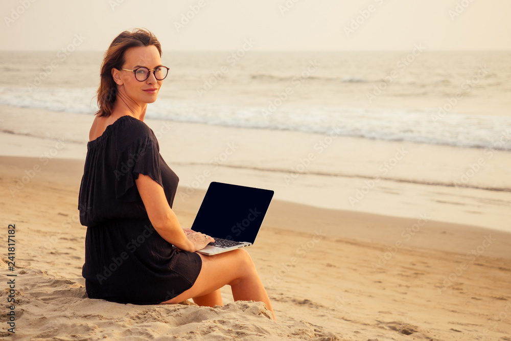 freelance and remote work.business woman in a stylish business summer suit with laptop sitting in the tropical ocean coast palm sand.female student with glasses online training education abroad