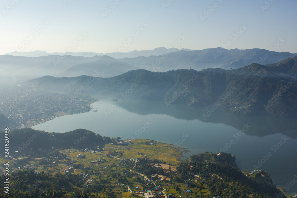 sunrise in a cloudy and foggy green mountain valley with a lake and a city on the shore