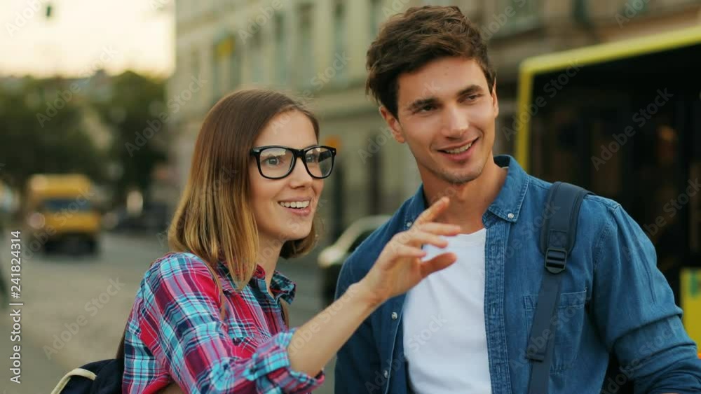 Young touristic couple standing on the street outdoors. Beautiful caucasian woman pointing hand in the direction to the landmark to visit.