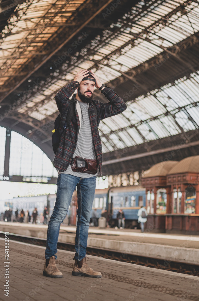 stylish bearded hipster tourist with backpack behind his shoulder on the platform of the railway station with a metal vault