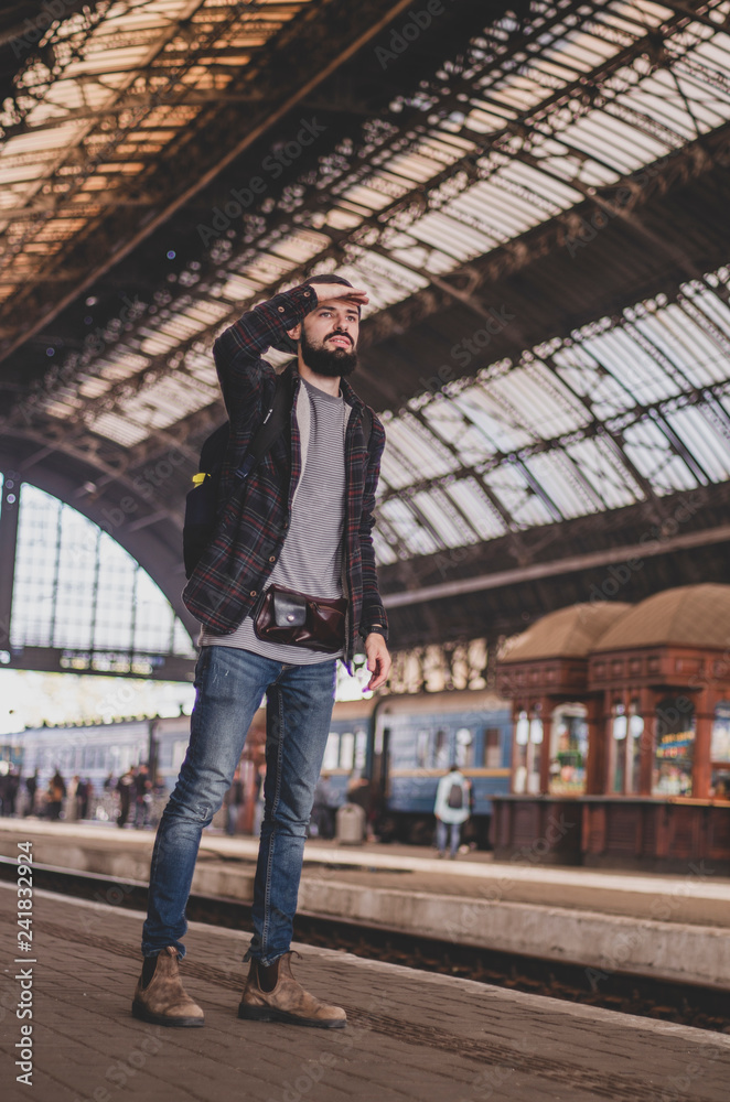 stylish bearded hipster tourist with backpack behind his shoulder on the platform of the railway station with a metal vault