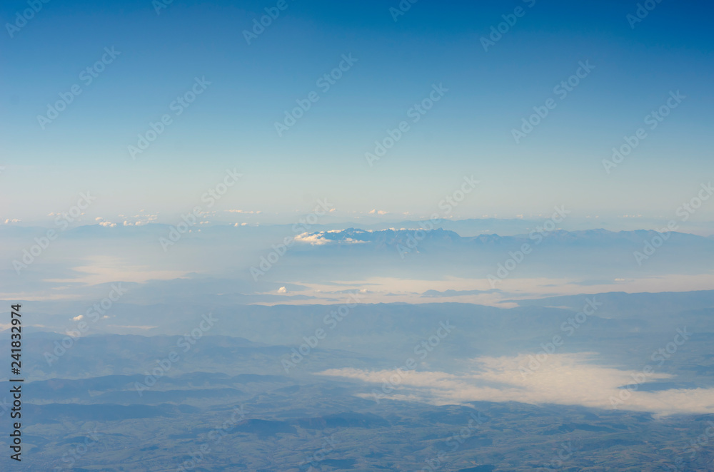 view from the window of the plane to the ground with mountains, rivers and horizon in the clouds and fog