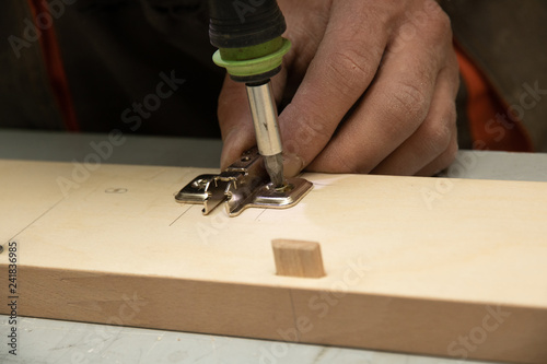 The furniture maker assemble a wardrobe, he is tightening the screws rechargeable screwdriver.