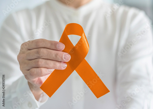 Orange ribbon for awareness on Leukemia, Kidney cancer, RDS disease, multiple sclerosis, ADHD illness, Chronic Obstructive Pulmonary Disease (COPD) in person's hand photo
