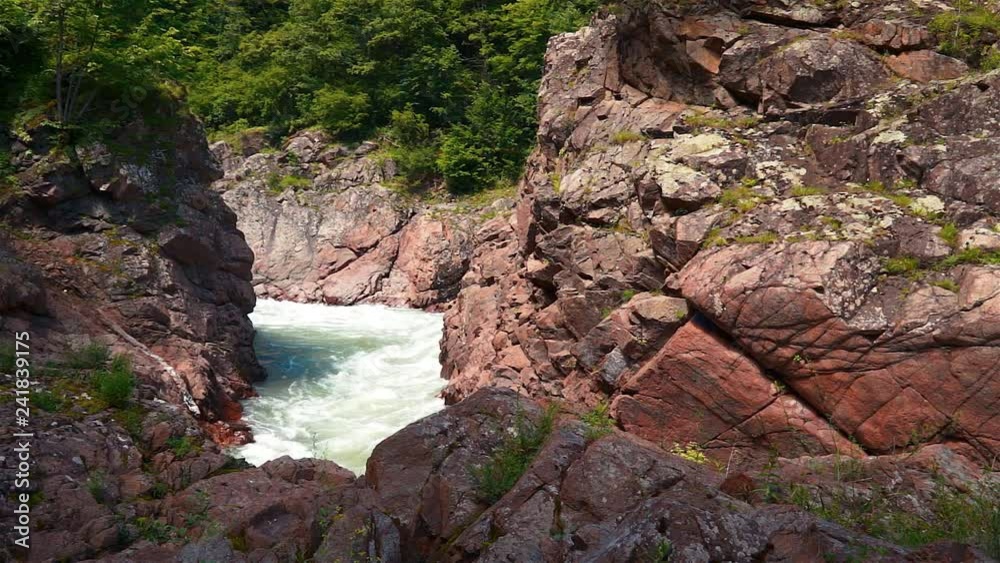 A stormy mountain river wags through the red rocks like a foamy stream. Mountains with green forest around. A stormy mountain river wags through the red rocks like a foamy stream. Mountains with green forest around.