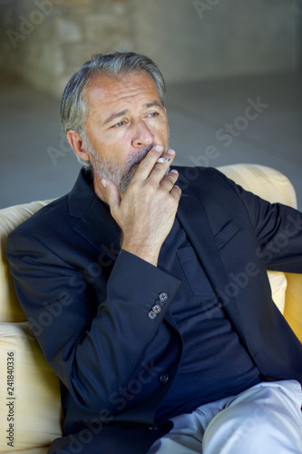 handsome adult man wearing blu jacket sitting and smoking on a sofa