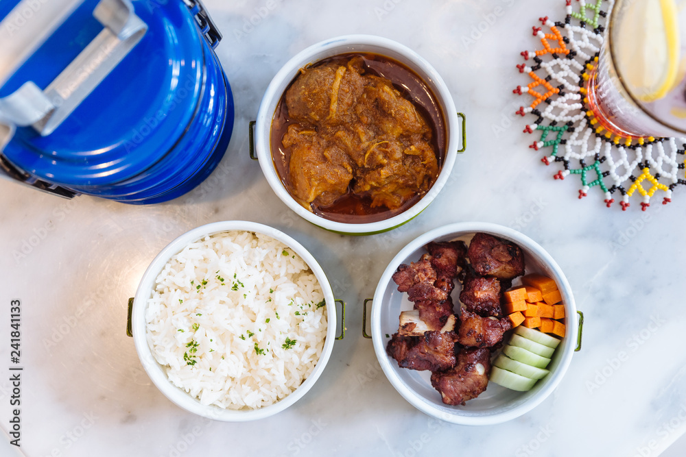 Thai food meal: Stream rice with parsley, Hang Lay Pork Curry and Stir fried spare rib pork with carrot and cucumber served in food carrier.
