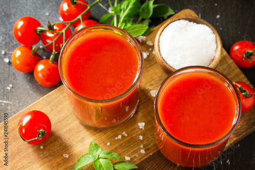 Diet nutrition concept. Glasses with tomato juice close-up and fresh tomatoes on a dark stone table.