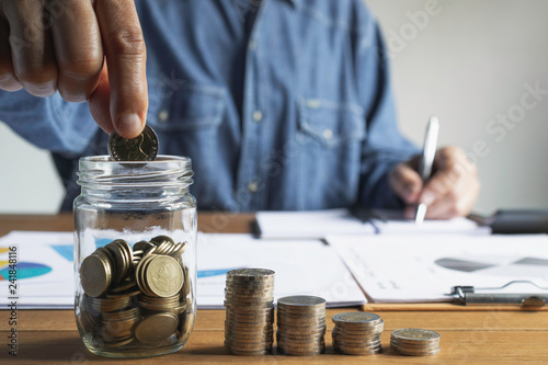 Business man putting the money in glass jar to saving,financial,accounting concept.